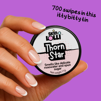 Hand holding a container of 'Thorn Star' by skin LOLLI against a purple background. headline reas 700 swipes in this itty bitty tin